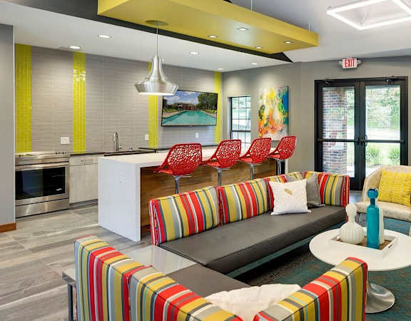 A modern living room with a striped couch and a kitchen area in the background. at Eden Commons, Eden Prairie, MN, 55344