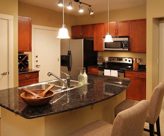 A kitchen with a black granite countertop and brown chairs.
