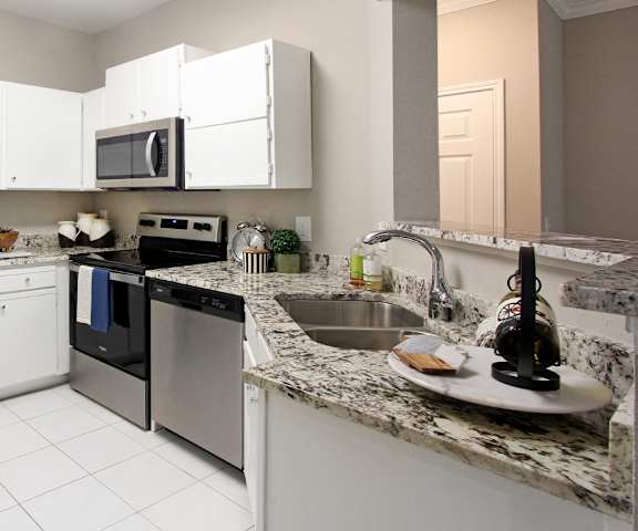 A kitchen with a refrigerator, microwave, oven, and sink.