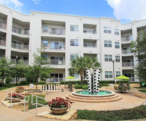A courtyard with a fountain and a green lawn in front of apartment buildings.