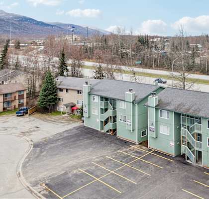 A parking lot in front of a green building with a mountain in the background.