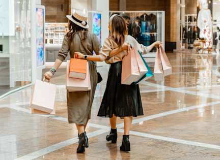 Two women walking in a mall carrying shopping bags.