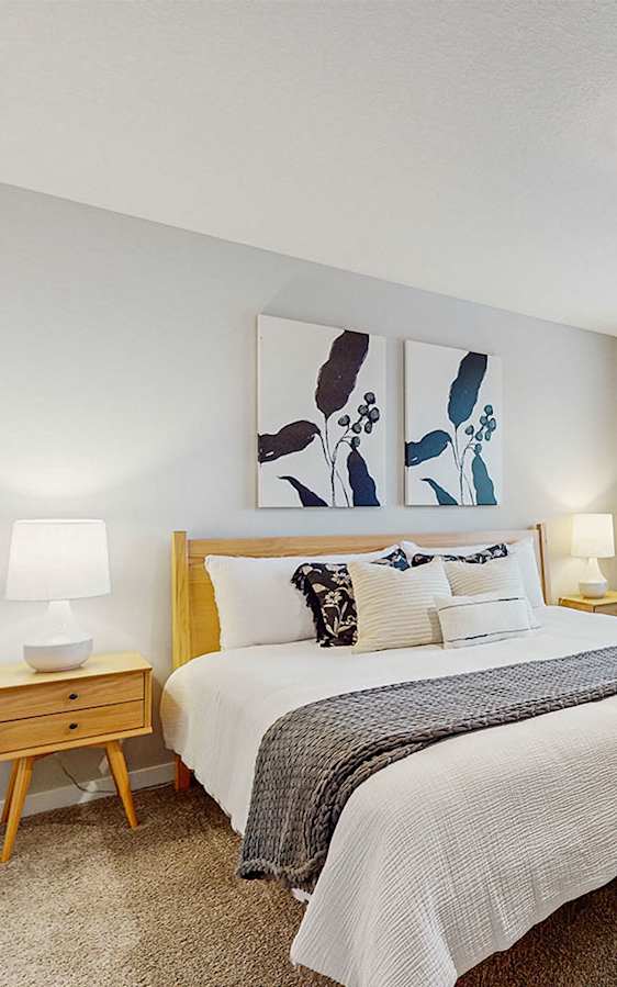 A bedroom with a bed, nightstand, and a painting on the wall.