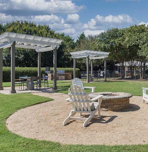 A park with a white gazebo, two white chairs and a table.