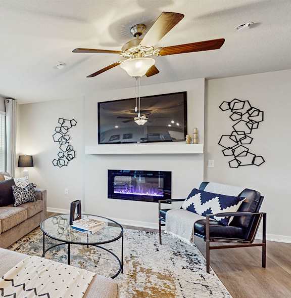 A living room with a couch, a chair, a coffee table, a fireplace, and a ceiling fan.