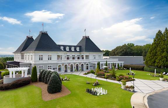 A large white mansion with a black roof and a flag on top.
