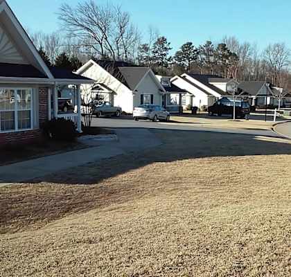 A grassy area with a sign and houses in the background.