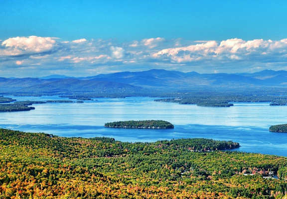 A serene landscape with a lake surrounded by mountains and trees in autumn colors.