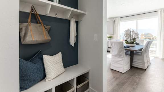 A room with a bench and a bag hanging on a hook.