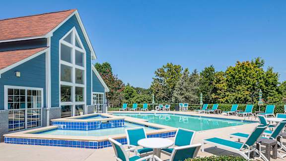 A pool with blue tiles and white chairs is in front of a blue building.