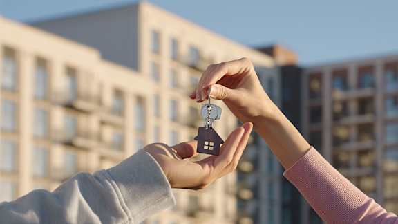 A person is handing over a key to another person in front of a building.