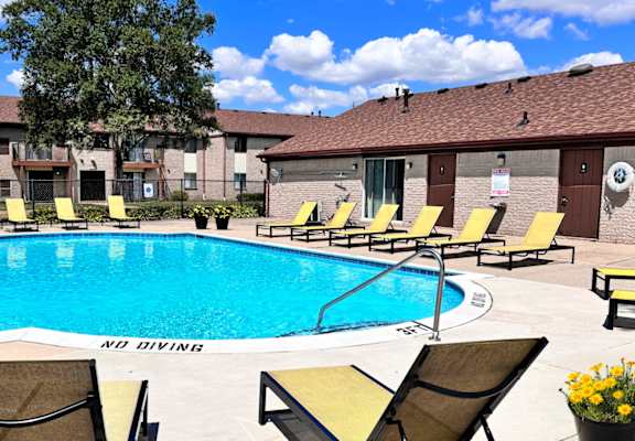 A pool surrounded by chairs and a building in the background.