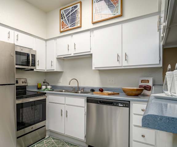 A kitchen with a refrigerator, microwave, oven, sink, and cabinets.