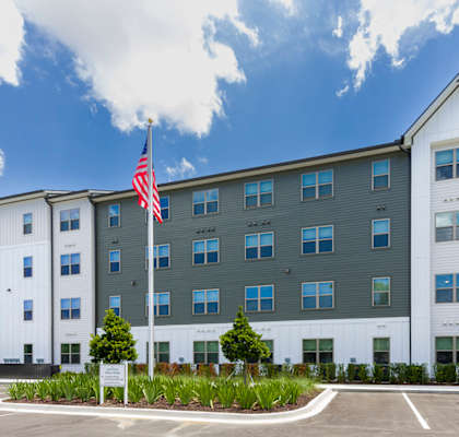 A large white building with a grey roof and a flag on the left side.