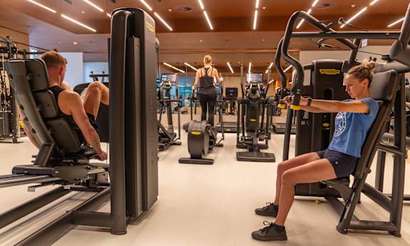 A gym with people working out and a woman doing a leg exercise.