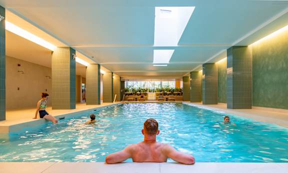 A man is sitting in a pool with his back to the camera.