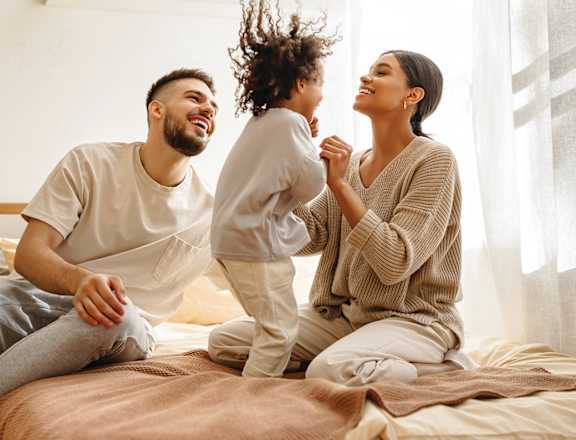 A man and woman sit on a bed with a small child at Tiburon Ridge, Omaha, NE 68136
