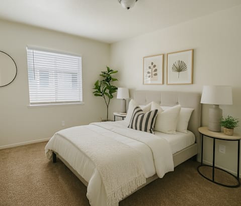 A bedroom with a bed, nightstand, and a plant.