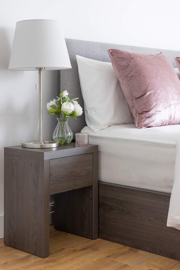 a bedroom with a bed and a nightstand with a lamp and flowers