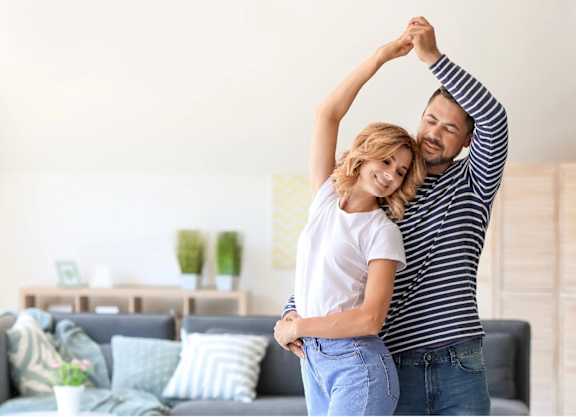 a man and woman standing in a living room with their arms in the air
