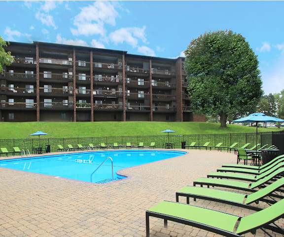 a swimming pool in front of a hotel with green lounge chairs
