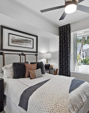 A bedroom with a large bed, a ceiling fan, and a window with blinds.