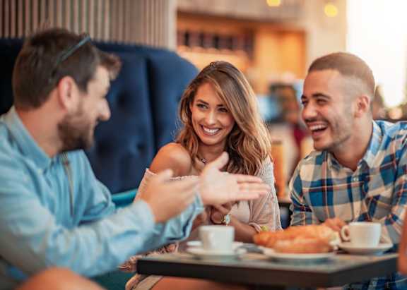 Three people are sitting at a table, laughing and enjoying a meal together.