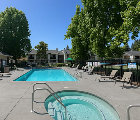 A swimming pool surrounded by chairs and trees.