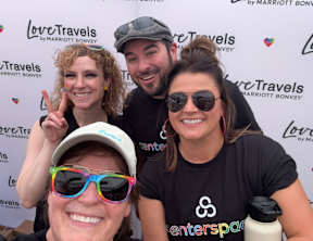Four people are standing in front of a backdrop for Love Travels by Marriott Bonvoy.