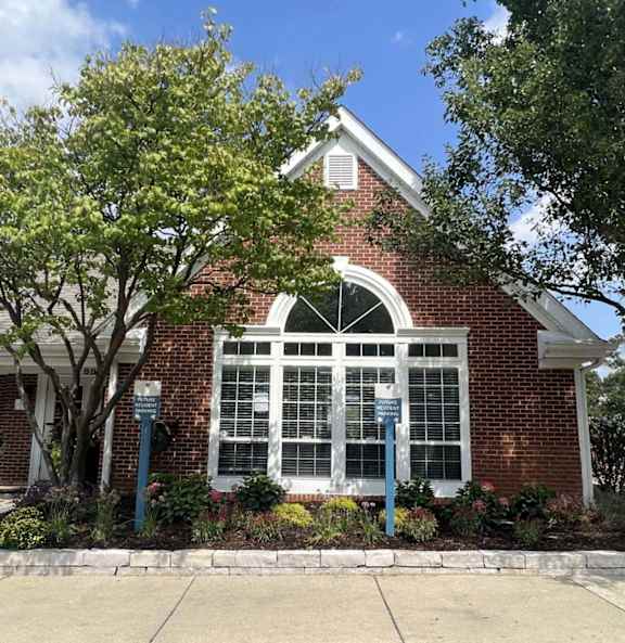 A red brick building with a white window and a tree in front.