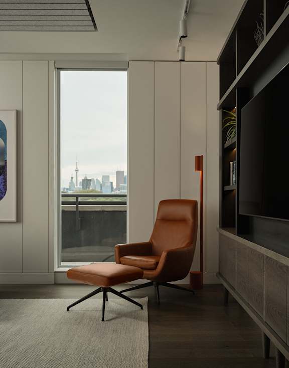 A brown chair is in front of a window with a city view.
