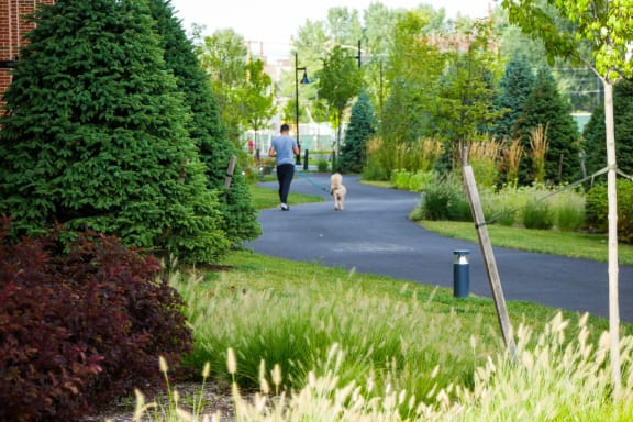 a woman walking her dog down a path in a park at 100 House Apartments, Jersey City , New Jersey