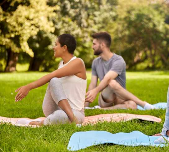 A group of people are sitting on yoga mats in a park.
