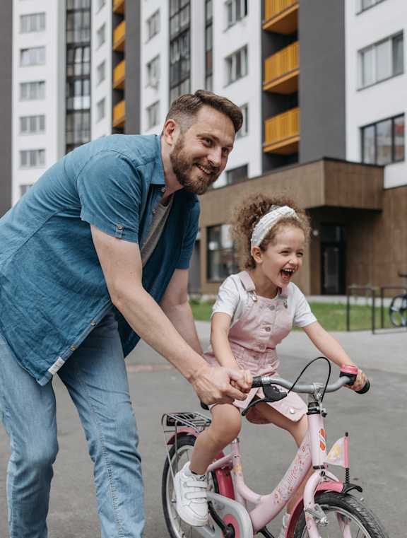 a man helping a little girl ride a bike