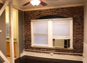 Thumbnail 7 of 29 - Living room in brookmore apartments in Pasadena featuring an exposed brick wall, large windows with shades, and a window air conditioning unit.