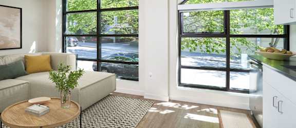 A living room with a couch, a table, and a window overlooking a street.