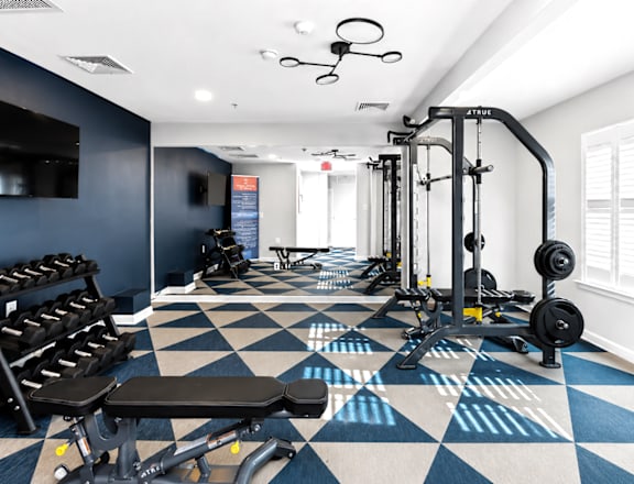 A gym with a variety of equipment including a bench press, squat rack, and dumbbells.