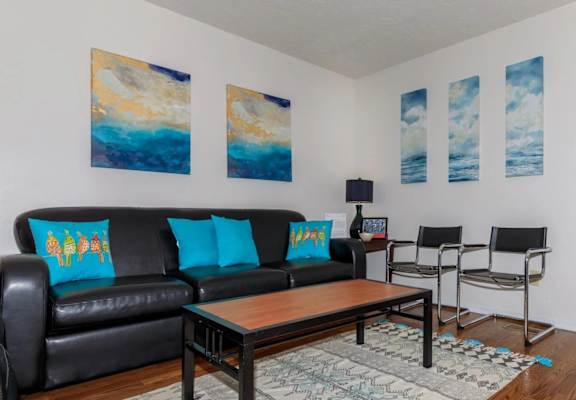 A living room with a black couch and a painting on the wall.