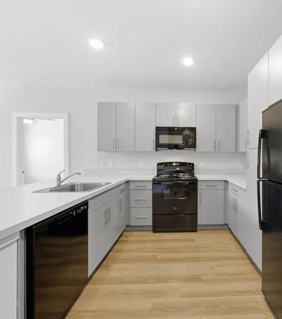 A room with a ceiling fan and a kitchen area with a fridge and microwave.