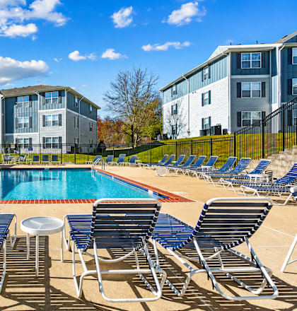 A pool surrounded by chairs and a building in the background.