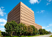 Thumbnail 2 of 4 - A large tan building with a lot of windows and trees in front of it.