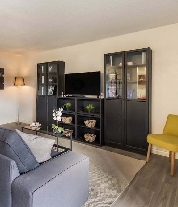 A grey couch sits in a living room with a yellow chair and a black cabinet.