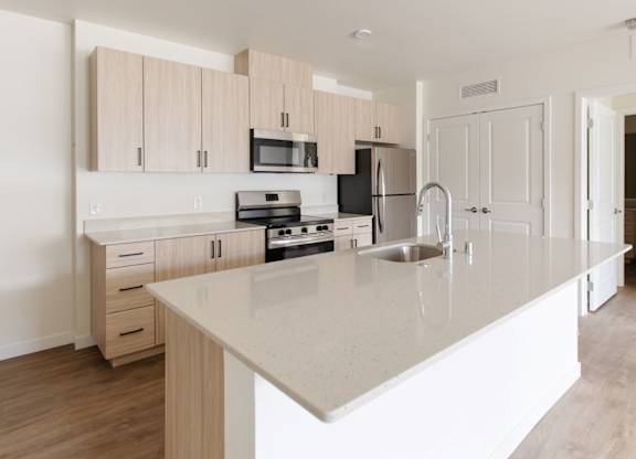 Modern apartment kitchen with large island, stainless steel appliances, and light wood cabinets at The Elowen in Lacey WA.