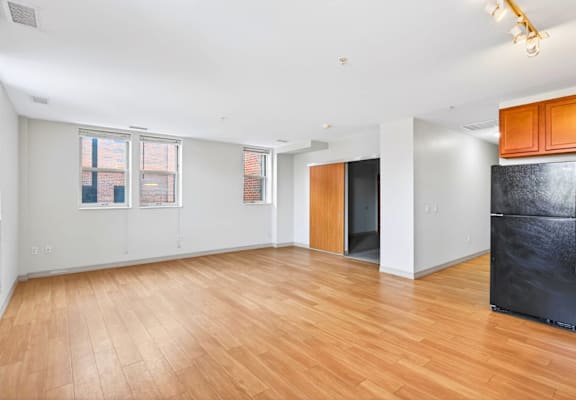 A spacious room with wooden flooring and a black refrigerator.
