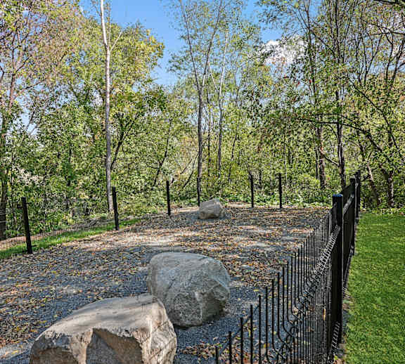A large rock sits in the middle of a gravel area in front of a black fence.