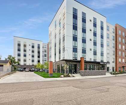 A row of modern apartment buildings with a parking lot in front.
