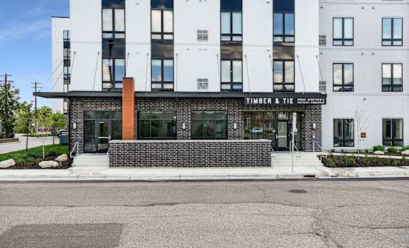 A Timber and Tie storefront with a brick pillar and a black awning.