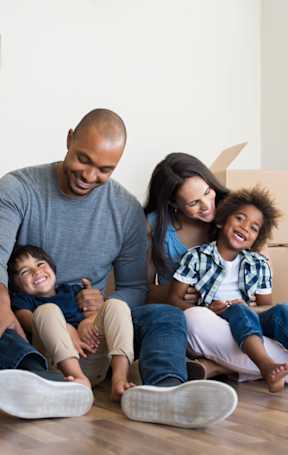 A family of four sitting on the floor surrounded by moving boxes.