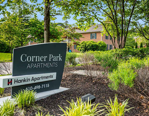 A sign for Corner Park Apartments sits in front of a green lawn.