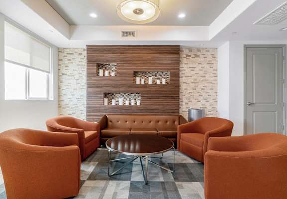 A modern living room with orange chairs and a brown sofa at The Adler Apartments, Los Angeles, California